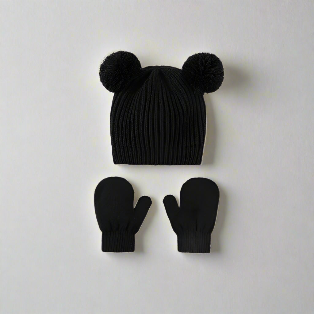 Black knit hat with pom-poms and matching mittens on a light gray background