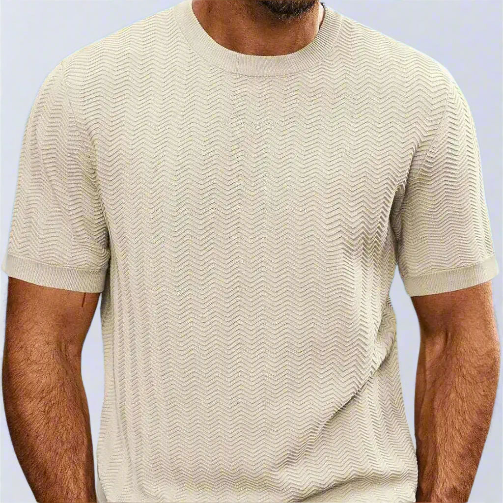 Man wearing a beige patterned t-shirt with a blurred beach background