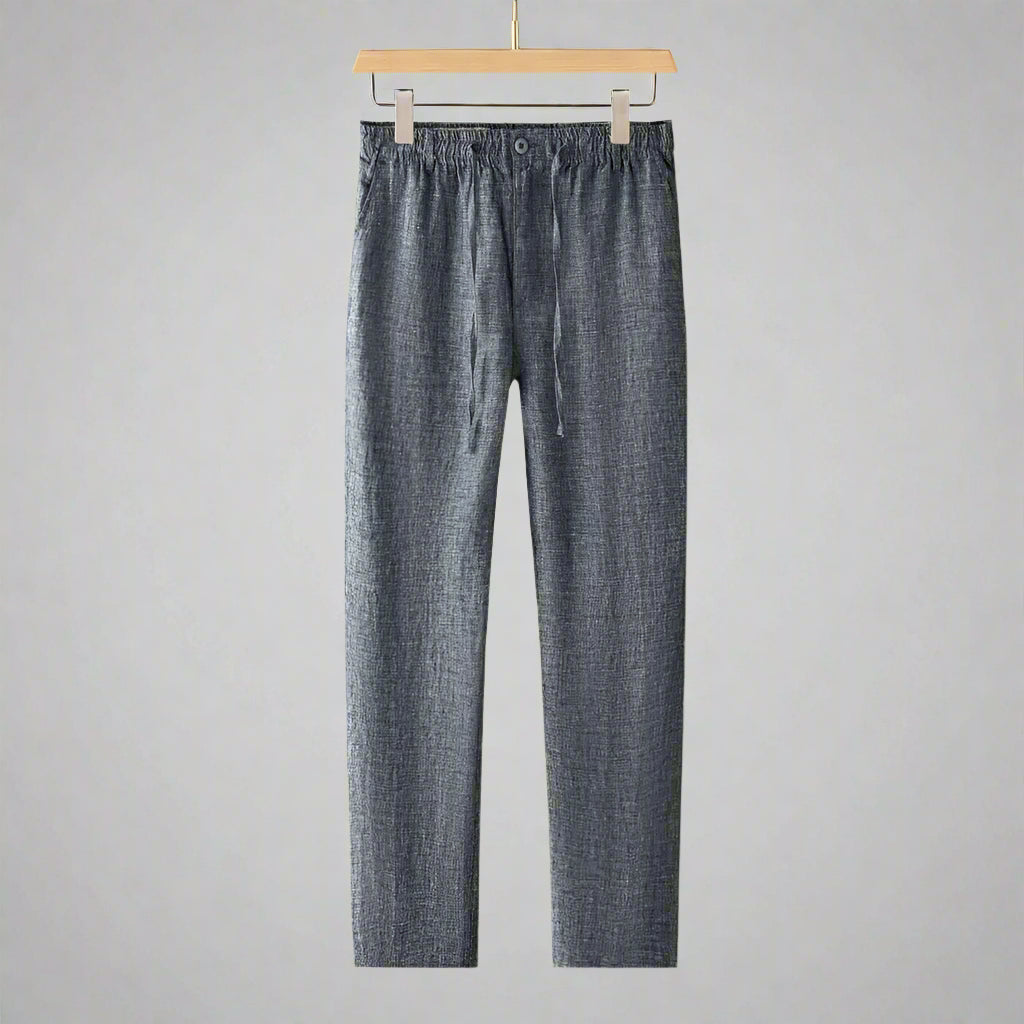 Blue denim pants hanging on a wooden hanger against a gray background