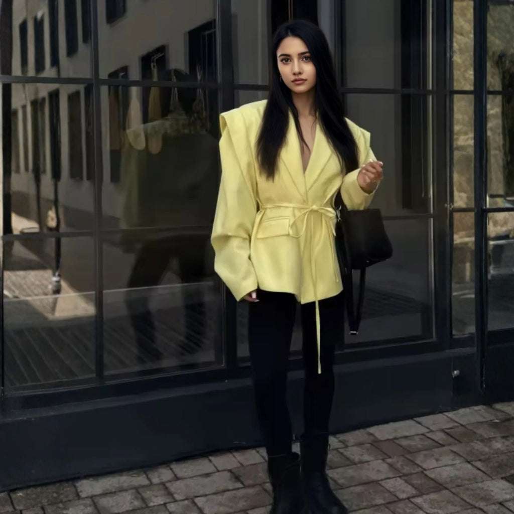 Woman in a yellow jacket standing in front of a reflective building.