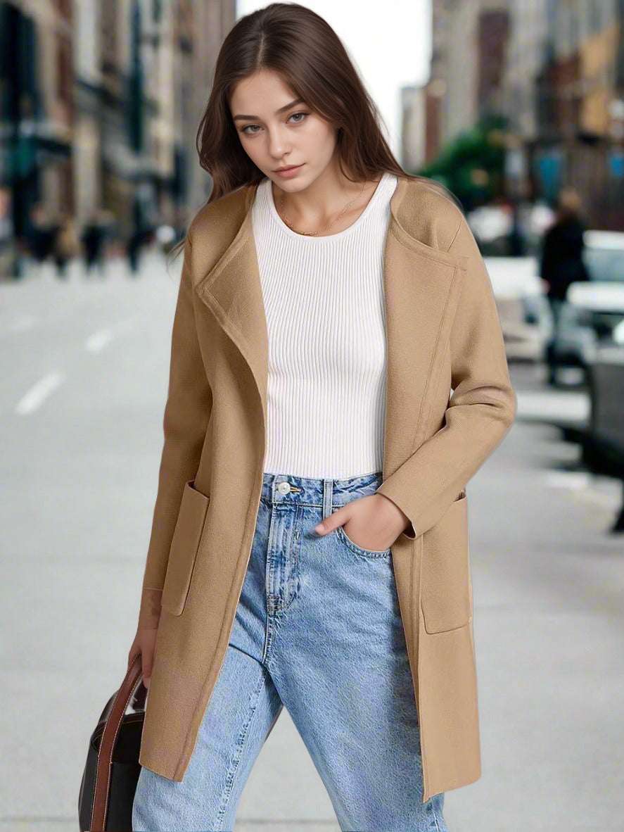 Woman wearing a beige coat, white sweater, and blue jeans on a city street.