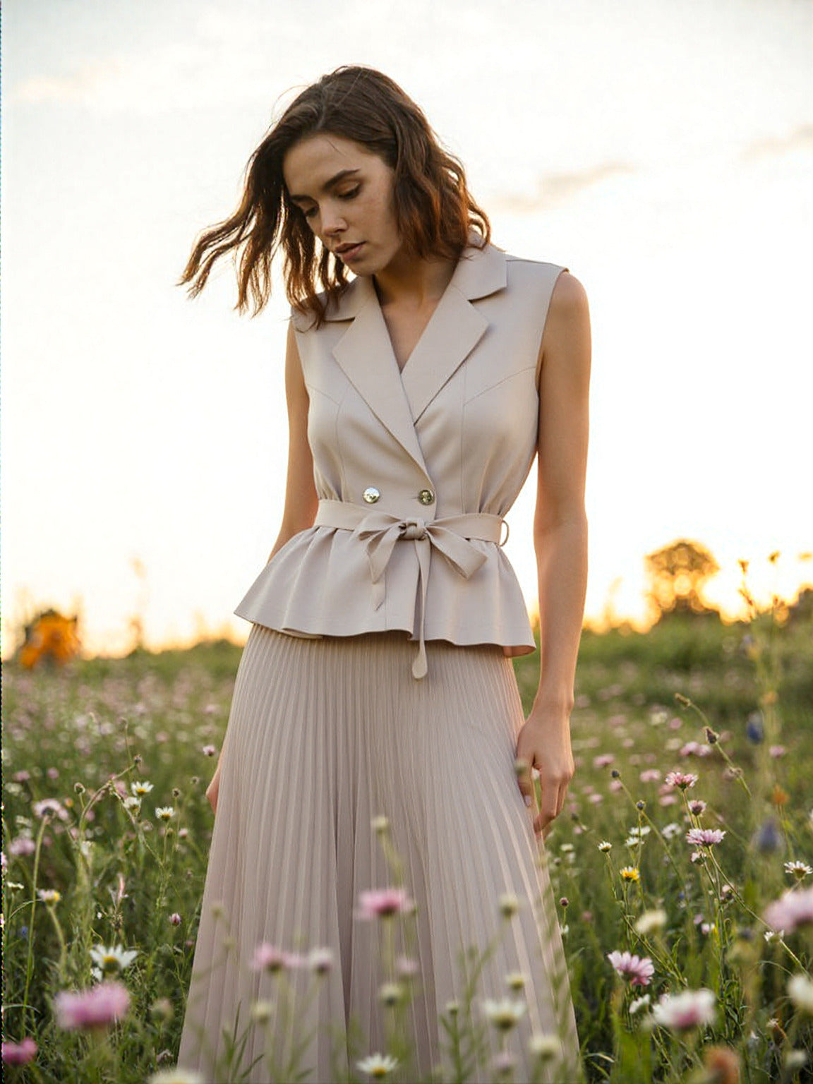 A woman standing in a field of grass and flowers in a beautiful earthly brown colored dress outfit.