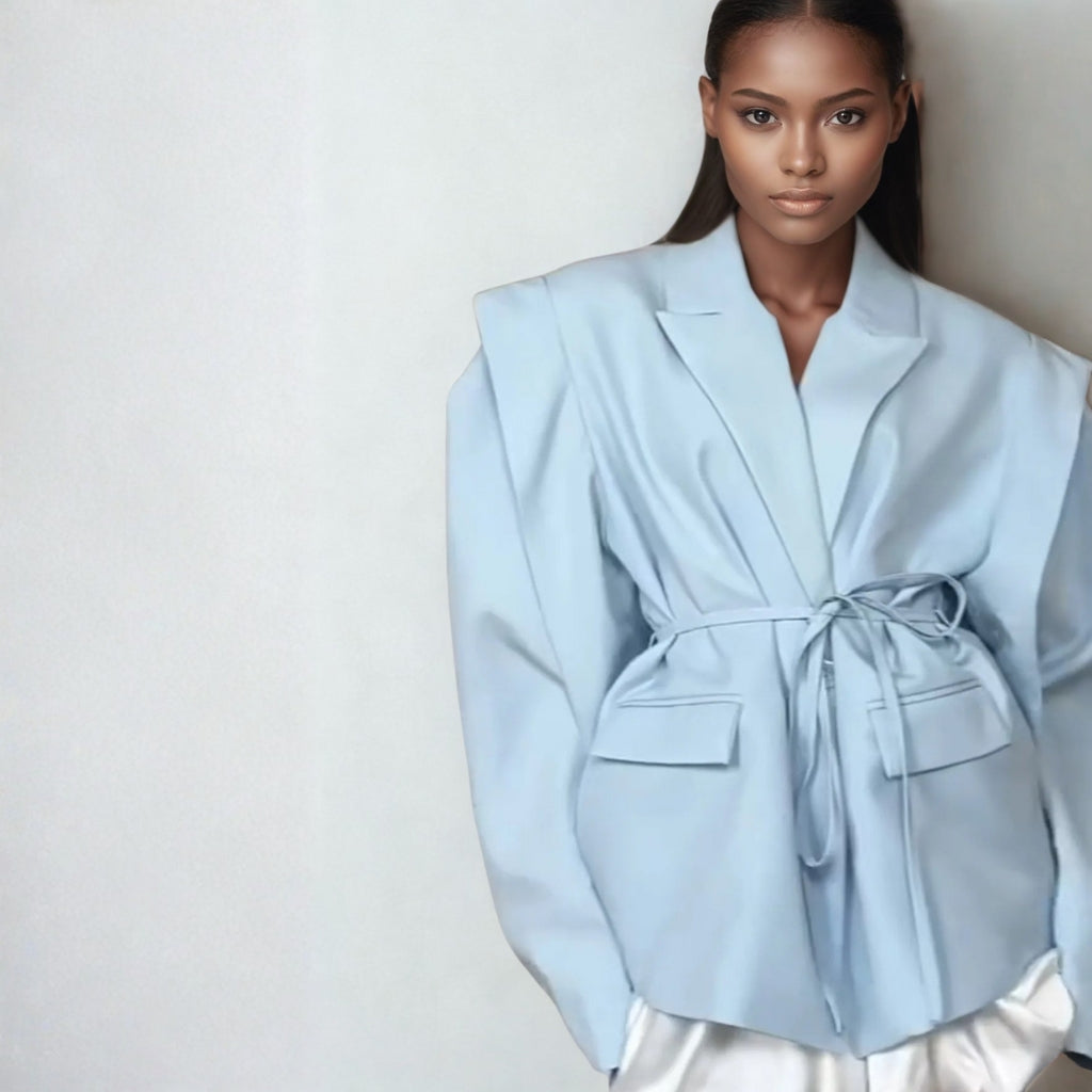 a woman model wearing a light blue oversized jacket and standing against white studio setting background