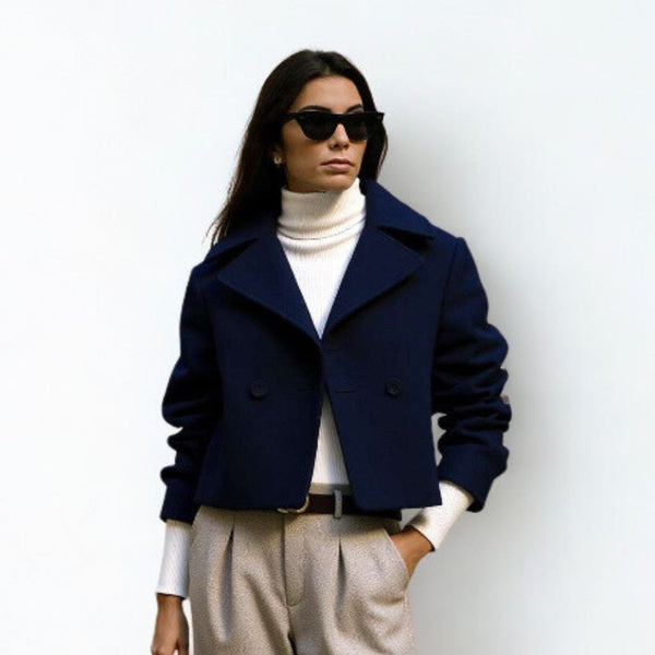A woman with sunglasses wearing modest warm blazer and white high neck sweater with light brown casual style pants. 