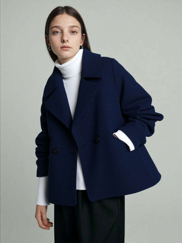 A woman wearing a dark blue short coat. Studio grey background.