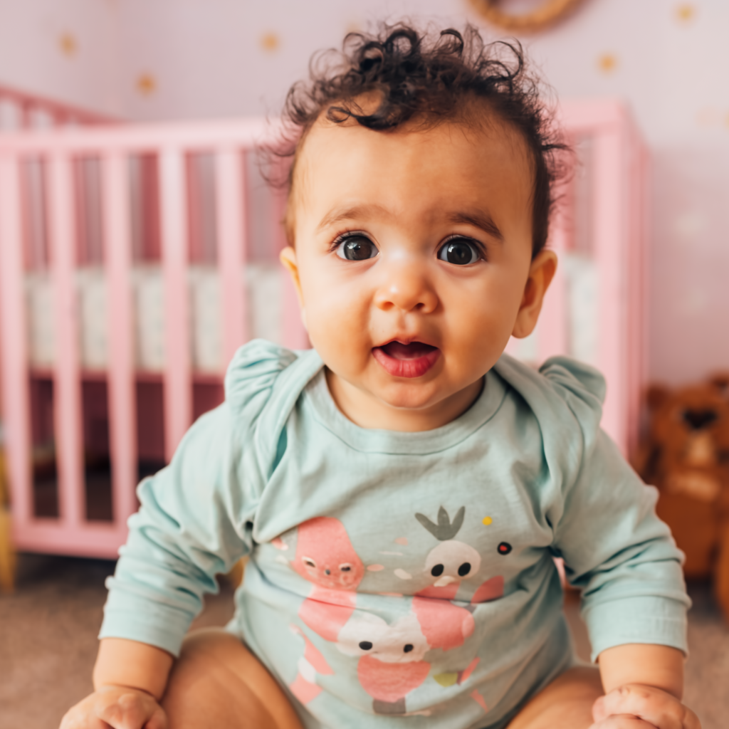 a cute baby posing in a light green romper with a pink crib in the background