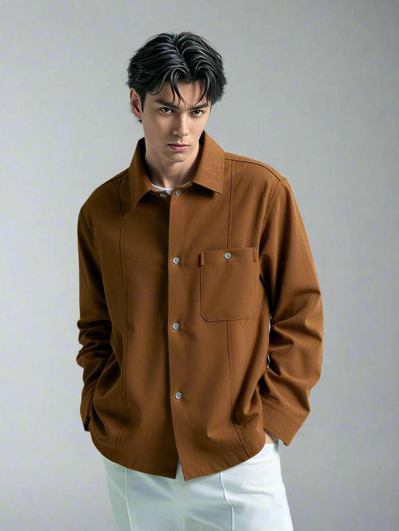 A man model wearing a brown suede button up shirt and standing against white studio setting background 