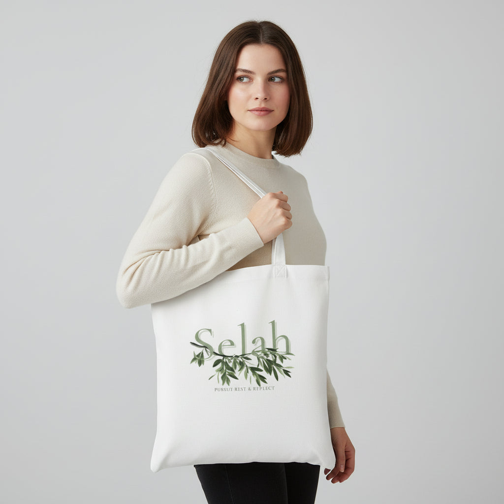 Woman holding a white tote bag with 'Selah' design on a light gray background