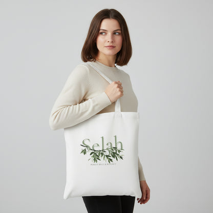 Woman holding a white tote bag with 'Selah' design on a light gray background