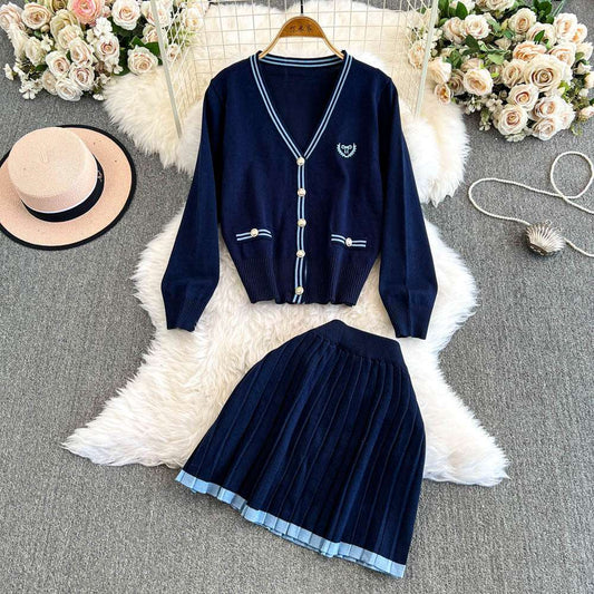 Navy blue cardigan and skirt set on a textured surface with flowers and a hat.