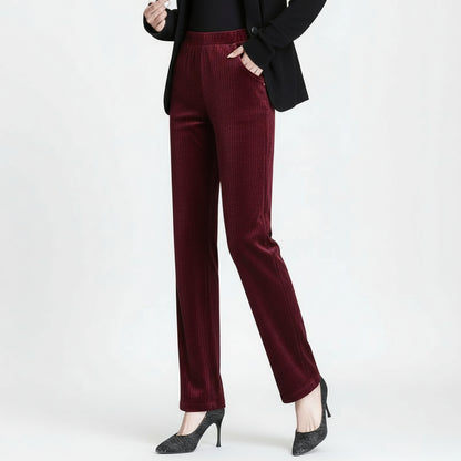 Burgundy velvet pants worn by a person on a gray background