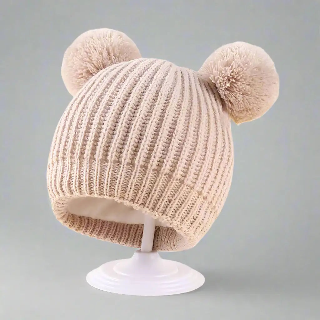 Beige knitted hat with two pom-poms on a white background