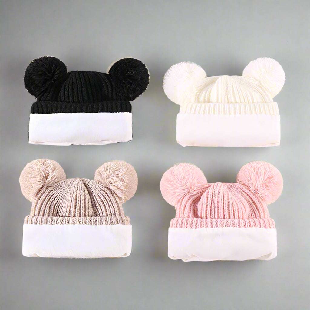 Four knitted hats with pom-pom ears on a beige background