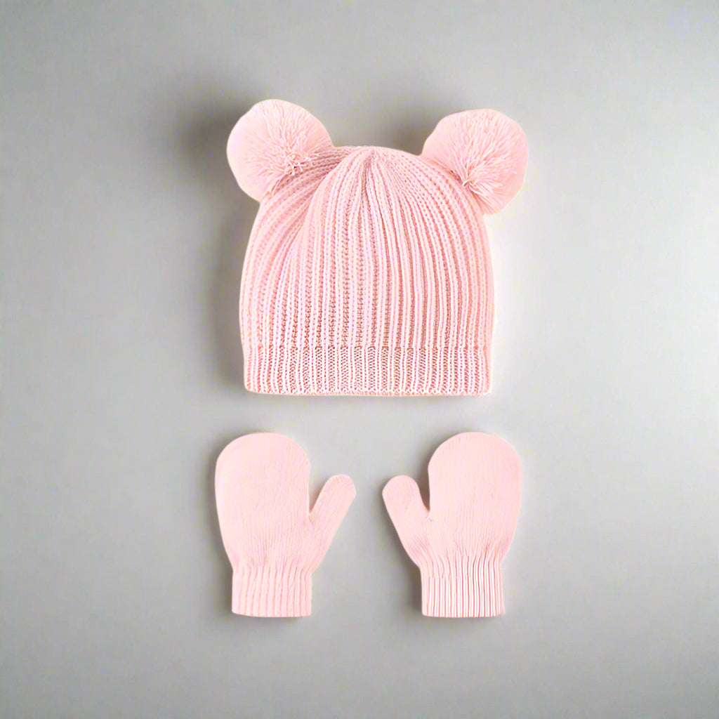 Pink knit hat with two pom-poms and matching mittens on a gray background