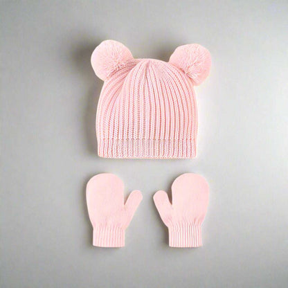 Pink knit hat with two pom-poms and matching mittens on a gray background