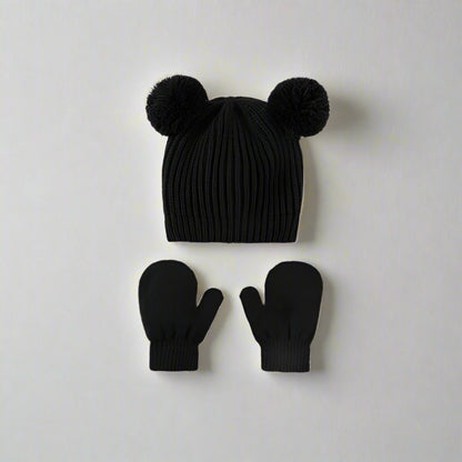 Black knit hat with pom-poms and matching mittens on a light gray background