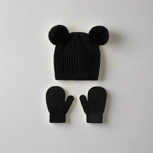 Black knit hat with pom-poms and matching mittens on a light gray background