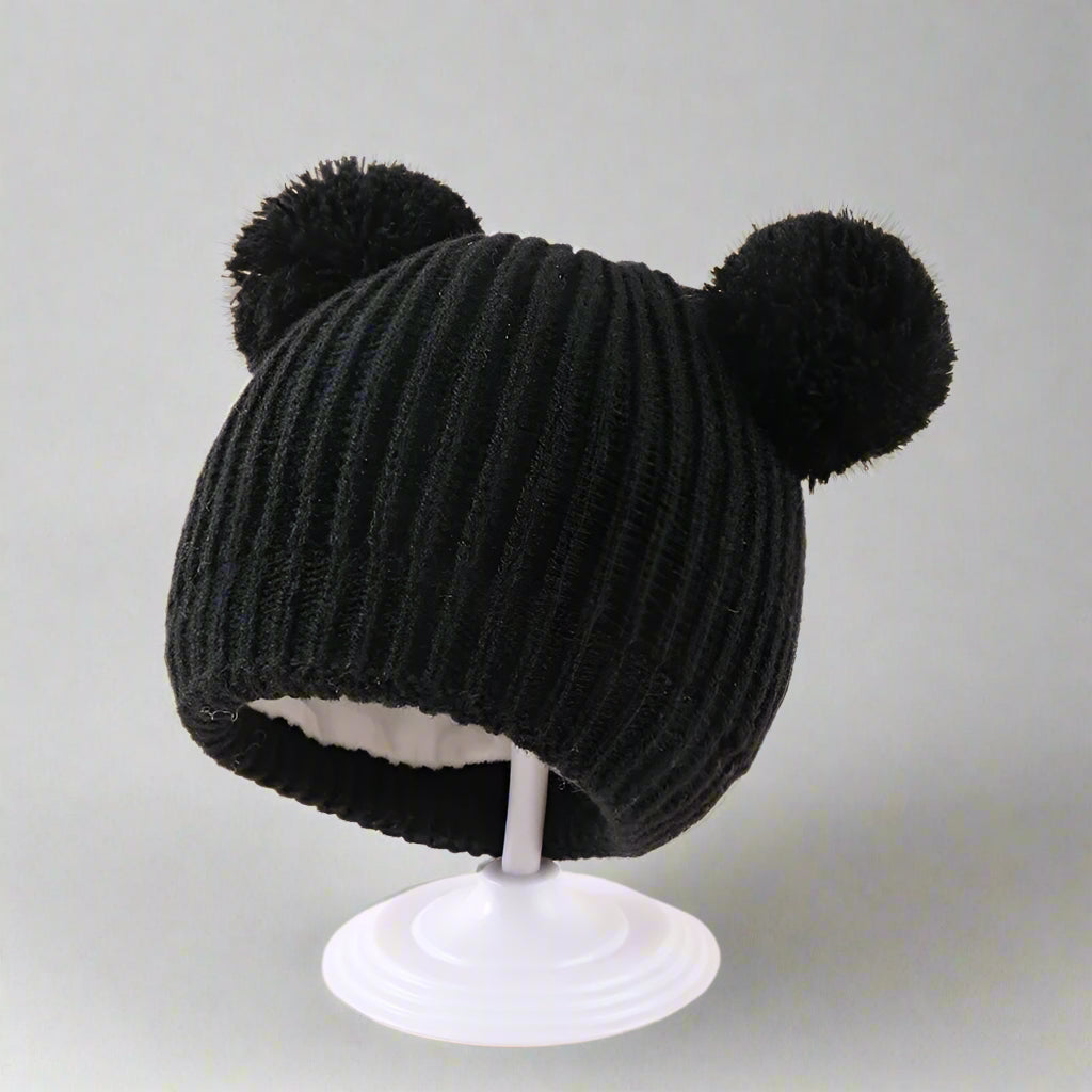 Black knitted hat with two pom-poms on a beige background