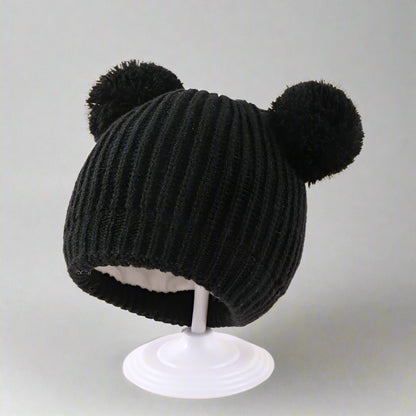 Black knitted hat with two pom-poms on a beige background