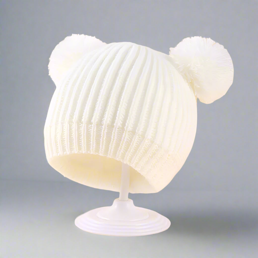 White knit beanie with a pom-pom on a beige background