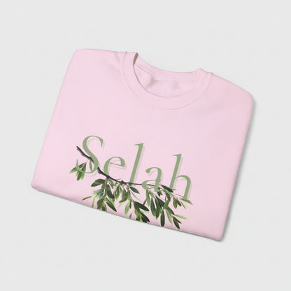 Folded pink sweatshirt with 'Selah' and green leaf design on a white background