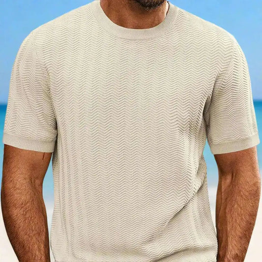 Man wearing a beige patterned t-shirt with a blurred beach background