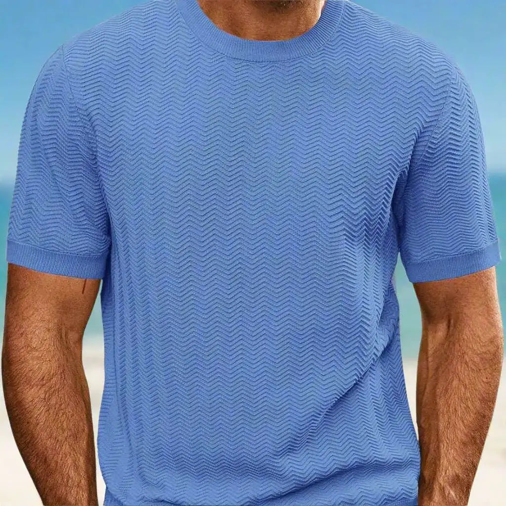 Person wearing a blue textured t-shirt with a blurred beach background