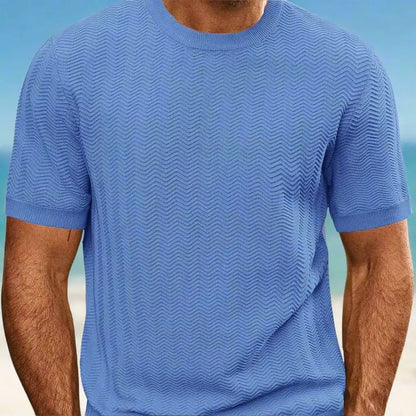 Person wearing a blue textured t-shirt with a blurred beach background
