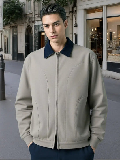 Man wearing a beige bomber jacket with a navy collar on a city street.