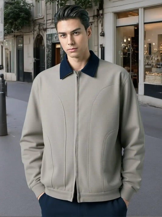 Man wearing a beige bomber jacket with a navy collar on a city street.