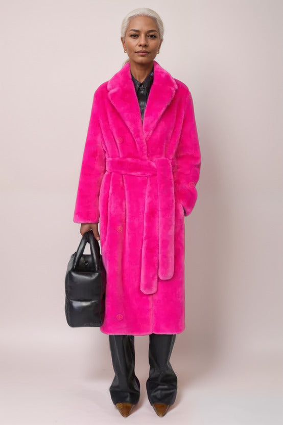 Model wearing a bright pink coat holding a black handbag against a plain background