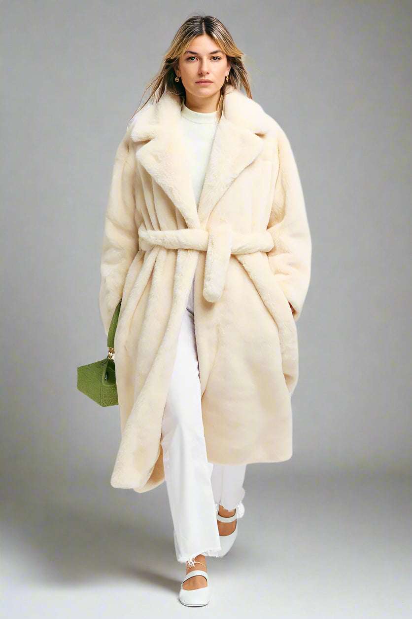 Woman wearing a long cream coat with a white background
