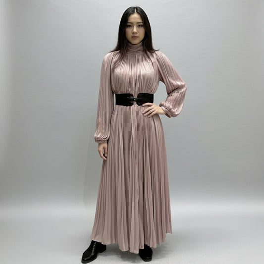 Woman wearing a long pink pleated dress with a black belt in a room with a yellow chair.