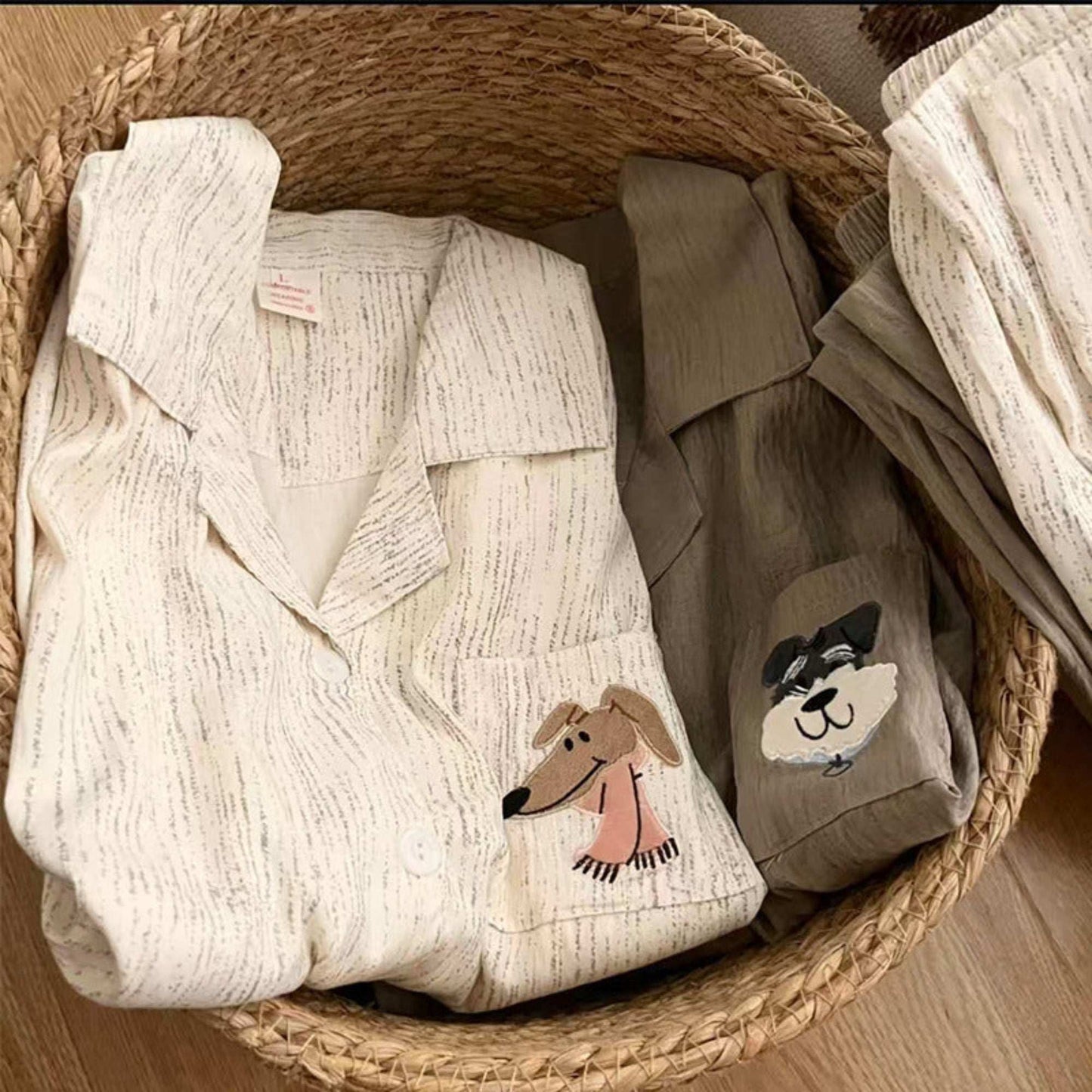 Woven basket with baby clothes, including a white outfit with dog design and brown pants with dog design.
