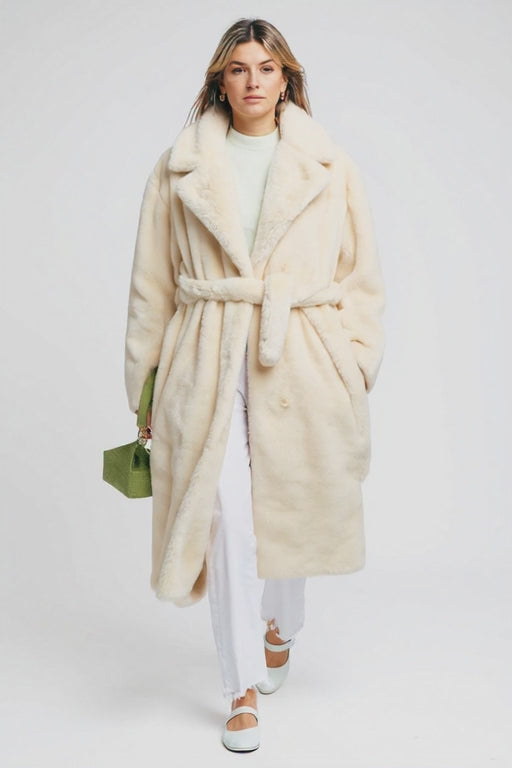 Woman wearing a long cream coat with a white background