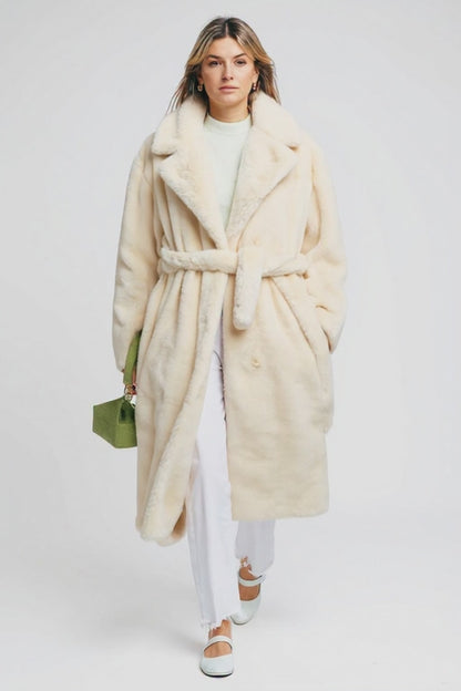 Woman wearing a long cream coat with a white background